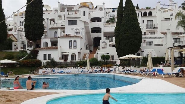 Une piscine avec des chaises longues et, en arrière-plan, un bâtiment à l’architecture blanche.