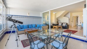 Een woonkamer met een telescoop, een bank, een glazen eettafel en een trap naar een andere kamer.