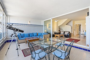 A living room with a telescope, a sofa, a glass dining table, and a staircase leading to another room.
