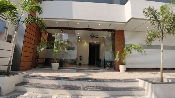 A modern building entrance with a glass facade, outdoor steps, and potted plants. - Hotel Yuvraj Palace (Bhopal)
