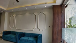 A modern living room with a large blue sofa set, a ceiling fan, recessed lighting, and a wooden accent wall. - Hotel Yuvraj Palace (Bhopal)