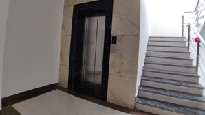 An elevator with a black frame and a control panel, adjacent to a staircase with metal railings and a red balloon. - Hotel Yuvraj Palace (Bhopal)