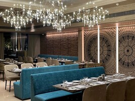 Un restaurante con asientos tapizados en azul, mesas dispuestas con platos y vasos, y un elemento decorativo de iluminación en el techo.