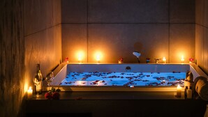 A bathtub with rose petals and candles, surrounded by wooden panels and a bottle of wine. - The Park Indore (Indore)