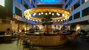 A modern bar area with a central wooden structure, multiple hanging lights, and surrounding seating. - The Park Indore (Indore)