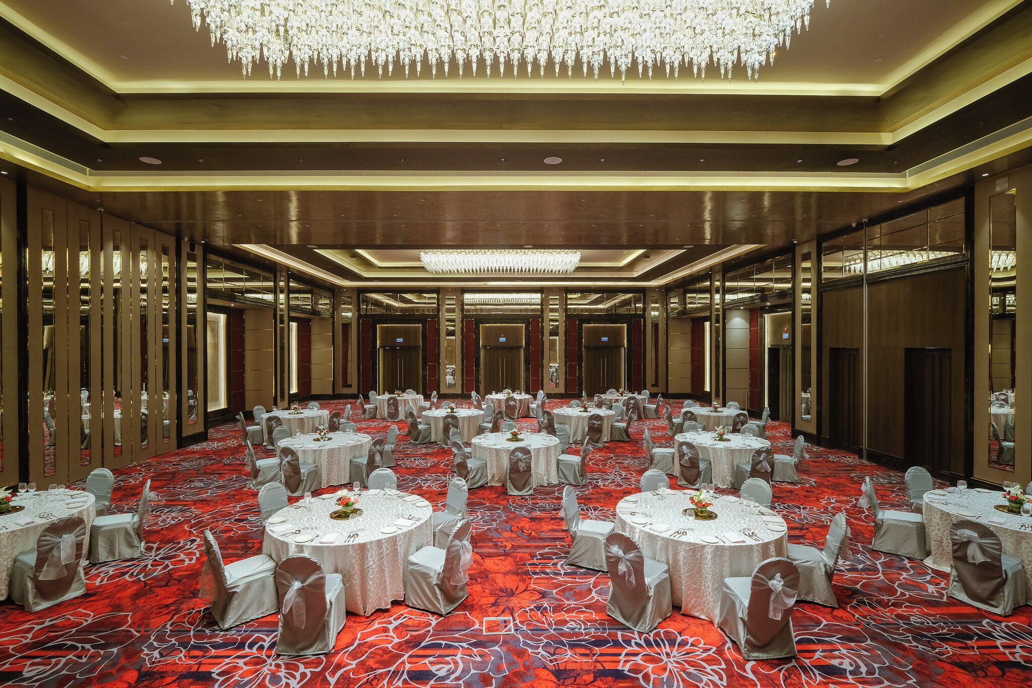 A large banquet hall with round tables, chairs, and a red carpet.