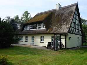 Ein traditionelles Fachwerkhäuschen mit Strohdach, einer Veranda und einem gepflegten Rasen.