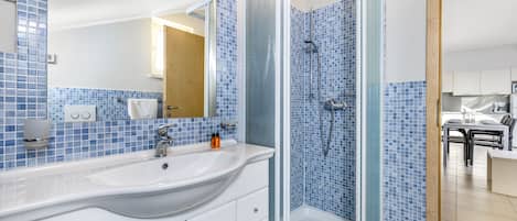 A bathroom with a glass-enclosed shower, a white sink, and blue-tiled walls.