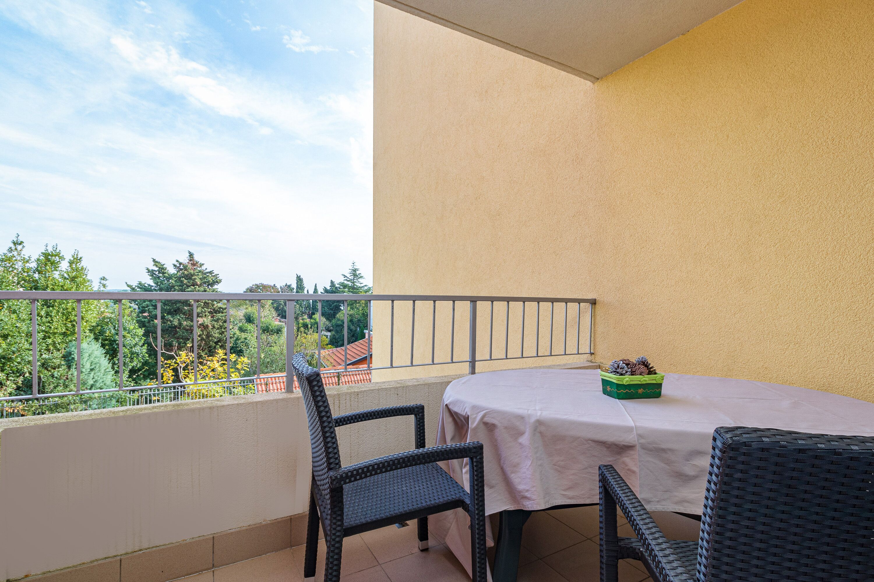 A balcony with a table and chairs, a potted plant, and a view of trees and buildings.