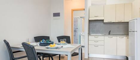 Una cucina compatta con mobili bianchi, un frigorifero e un'area pranzo con tavolo e sedie.