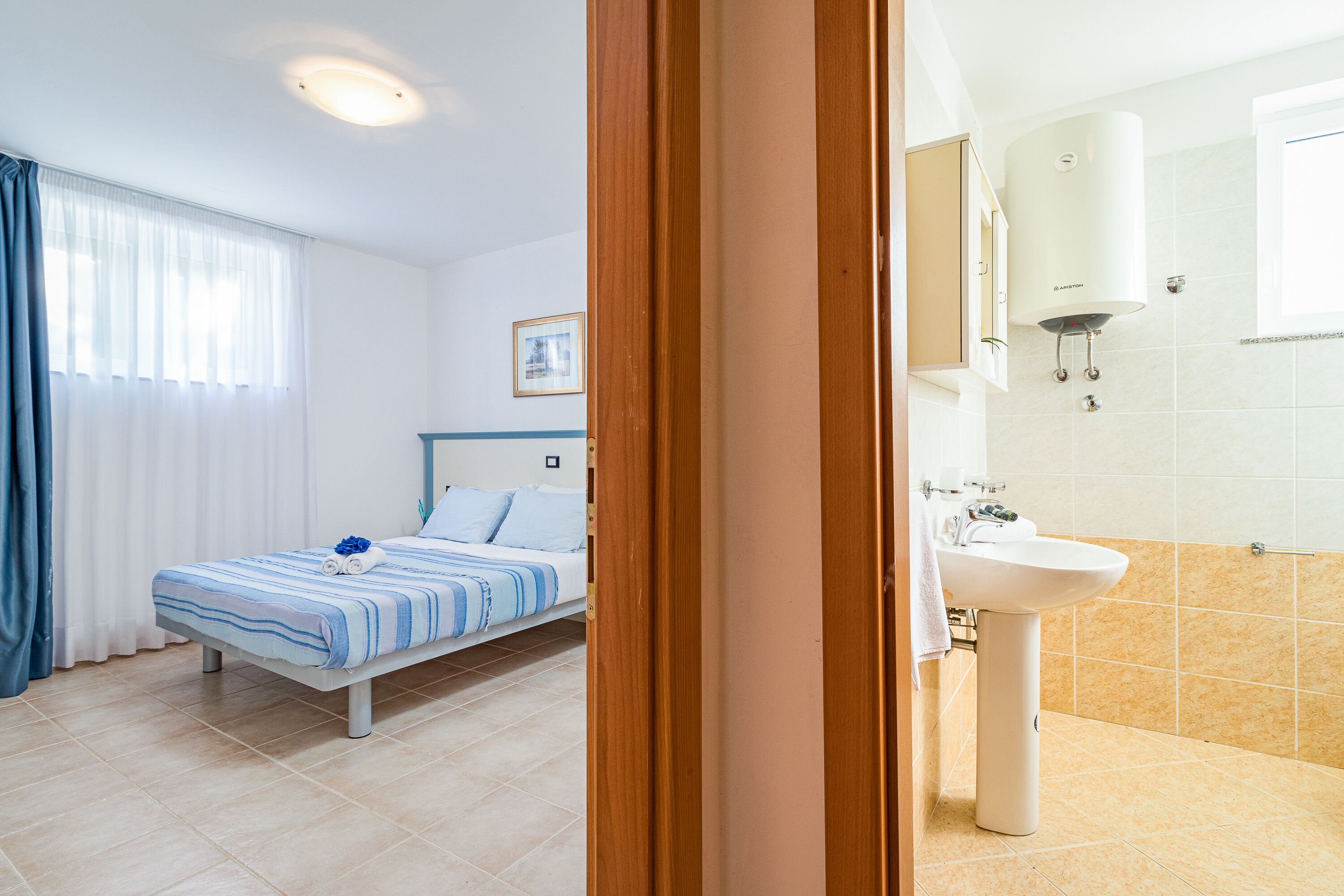 Camera d'albergo con un letto, un bagno con lavandino e specchio, e una finestra con tende.