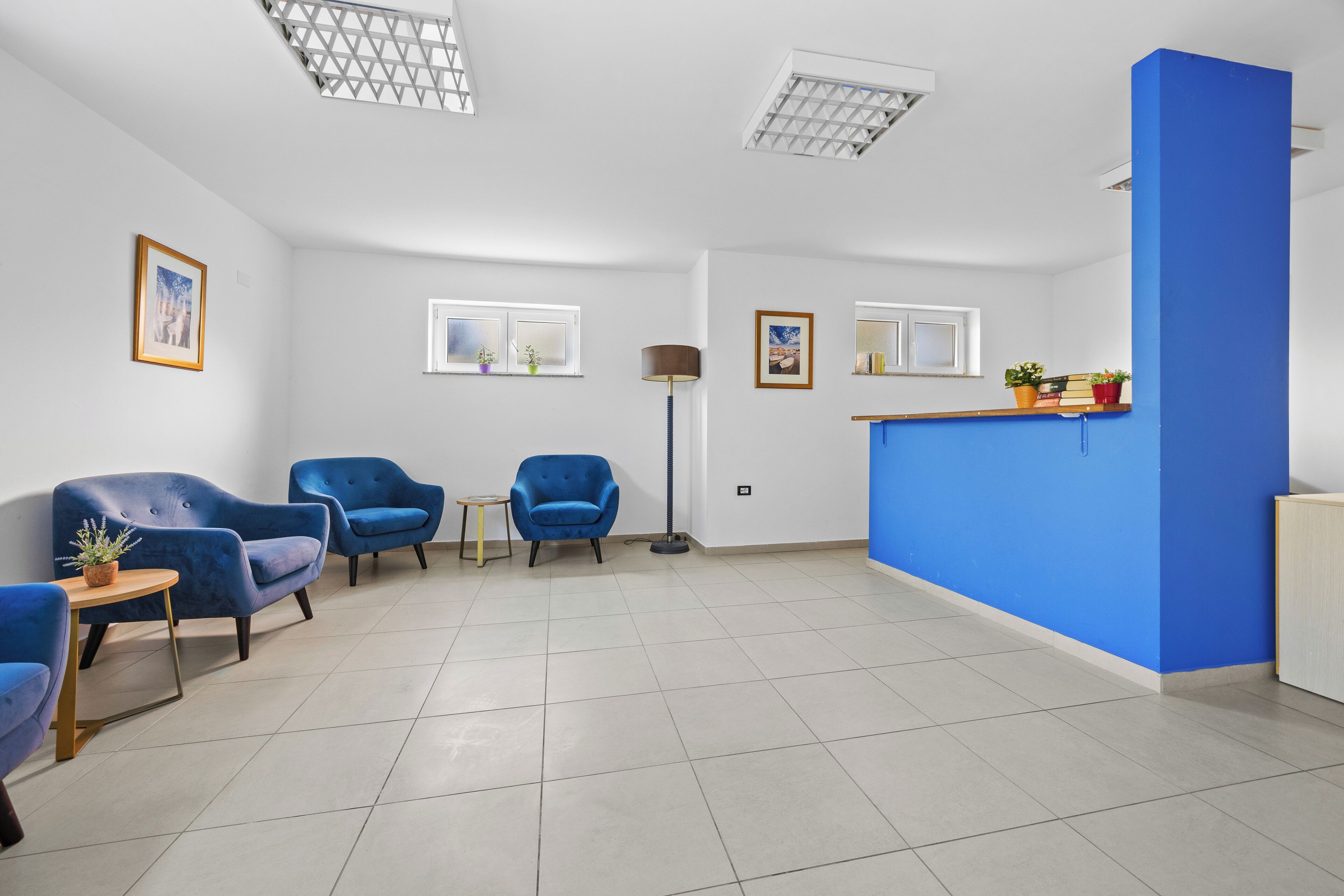 A modern reception area with a blue accent wall, a reception desk, and seating arrangements including a blue armchair and a small table with a plant.