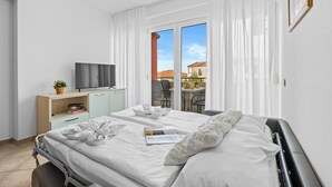 A hotel room with a bed, a television, a desk with a plant, and a view of the outside. - Residence Kamenjak (Medulin)
