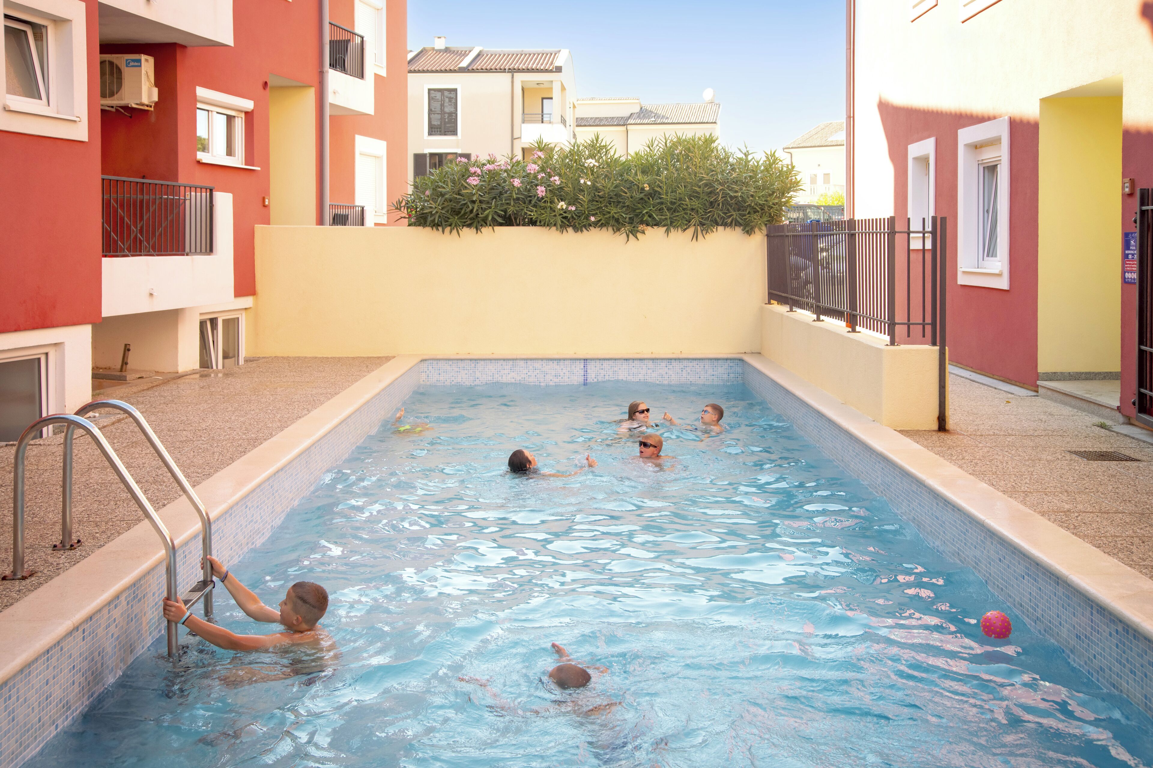 Une piscine avec des personnes à l’intérieur, entourée d’immeubles.