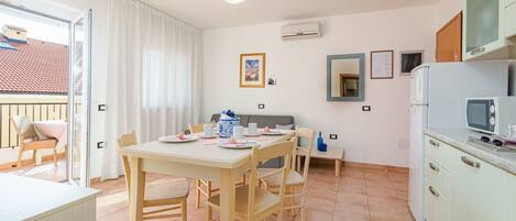 A compact kitchen with a dining area, a small refrigerator, and a window with curtains.