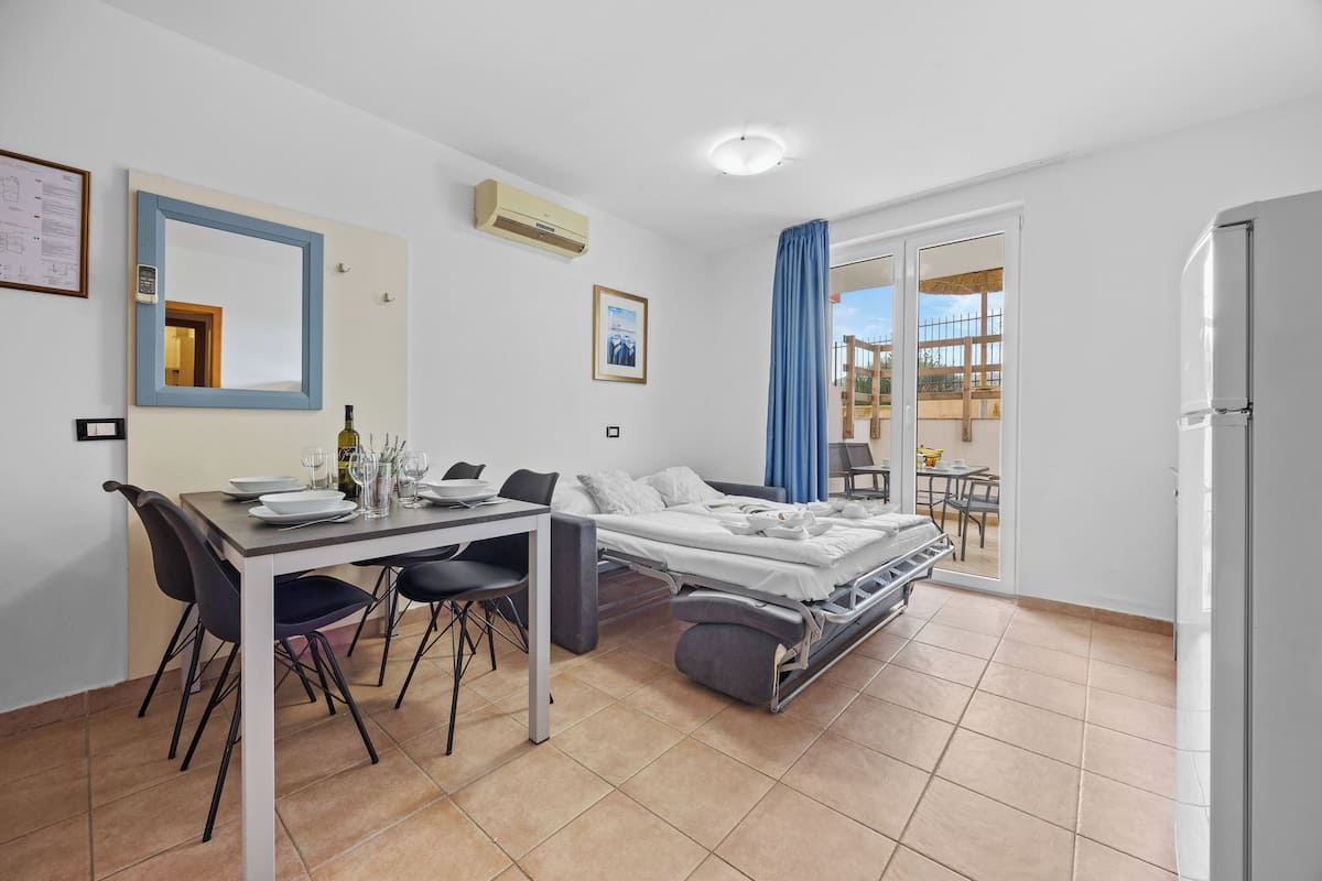 A modern bedroom with a bed, a dining table with chairs, and a small balcony with a table and chairs.