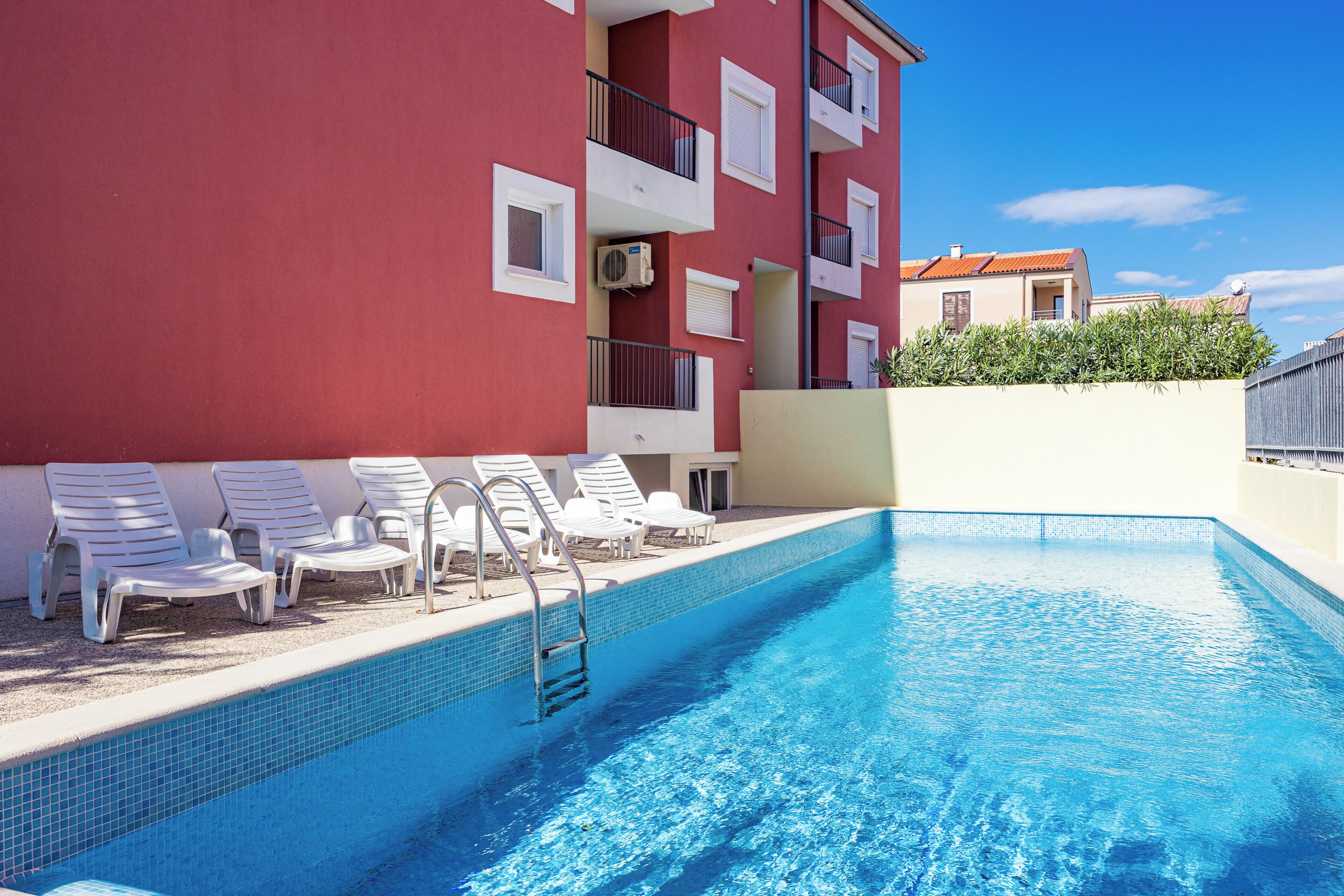 A swimming pool with white lounge chairs and a red building in the background.