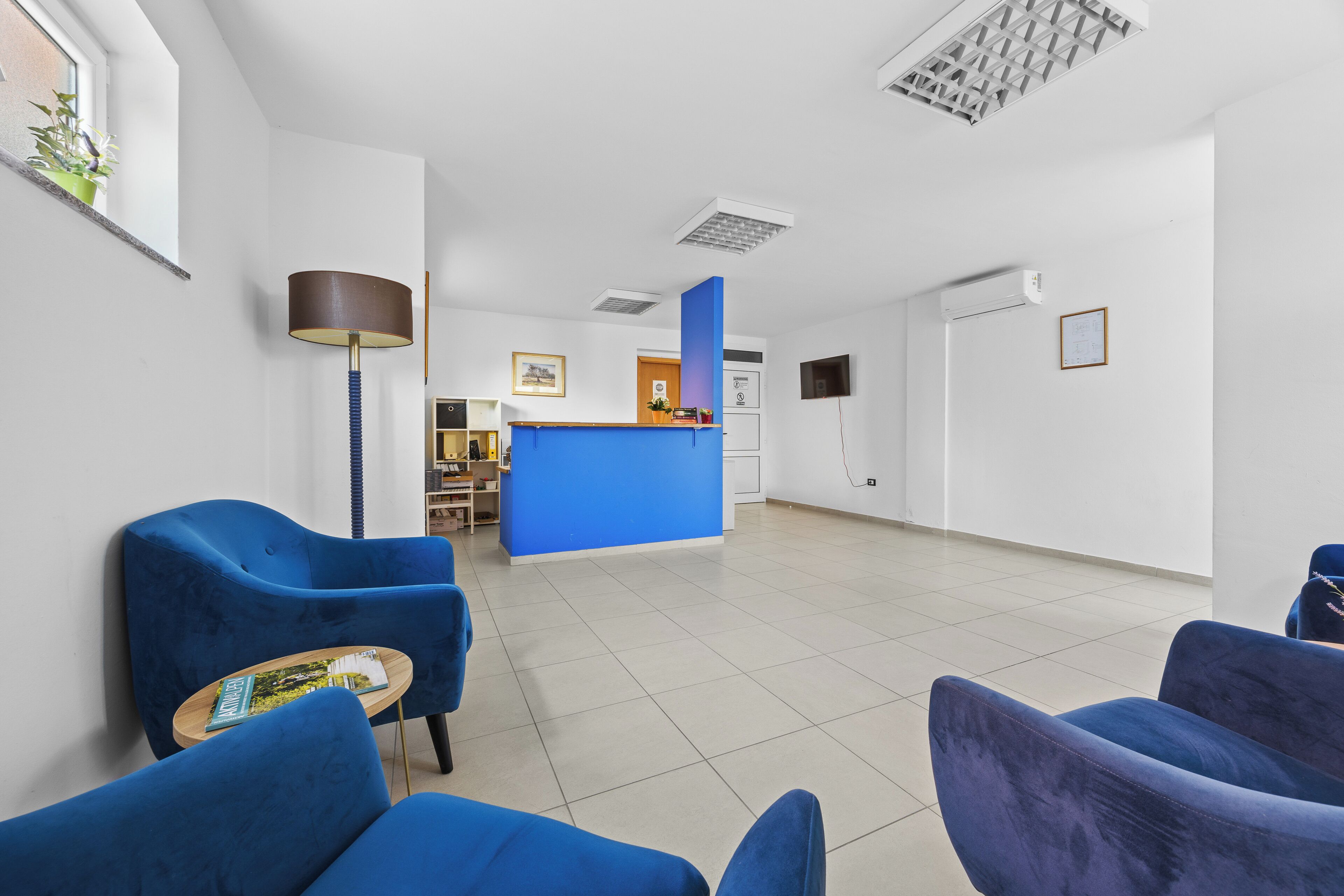 Un espace d’accueil avec un comptoir bleu, des chaises bleues, une lampe et un sol carrelé.
