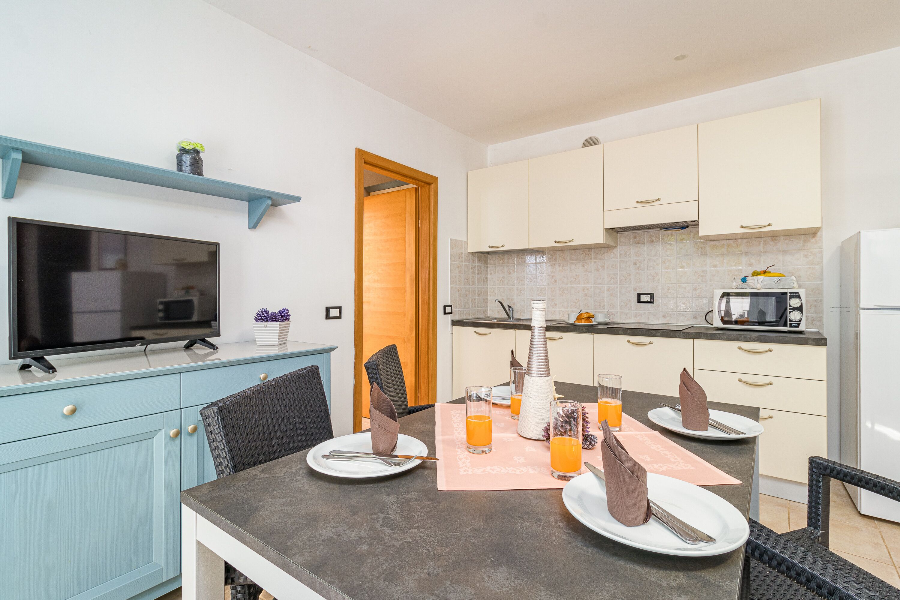 Una cocina moderna con una mesa de comedor preparada para cuatro personas, un televisor de pantalla plana y un microondas.