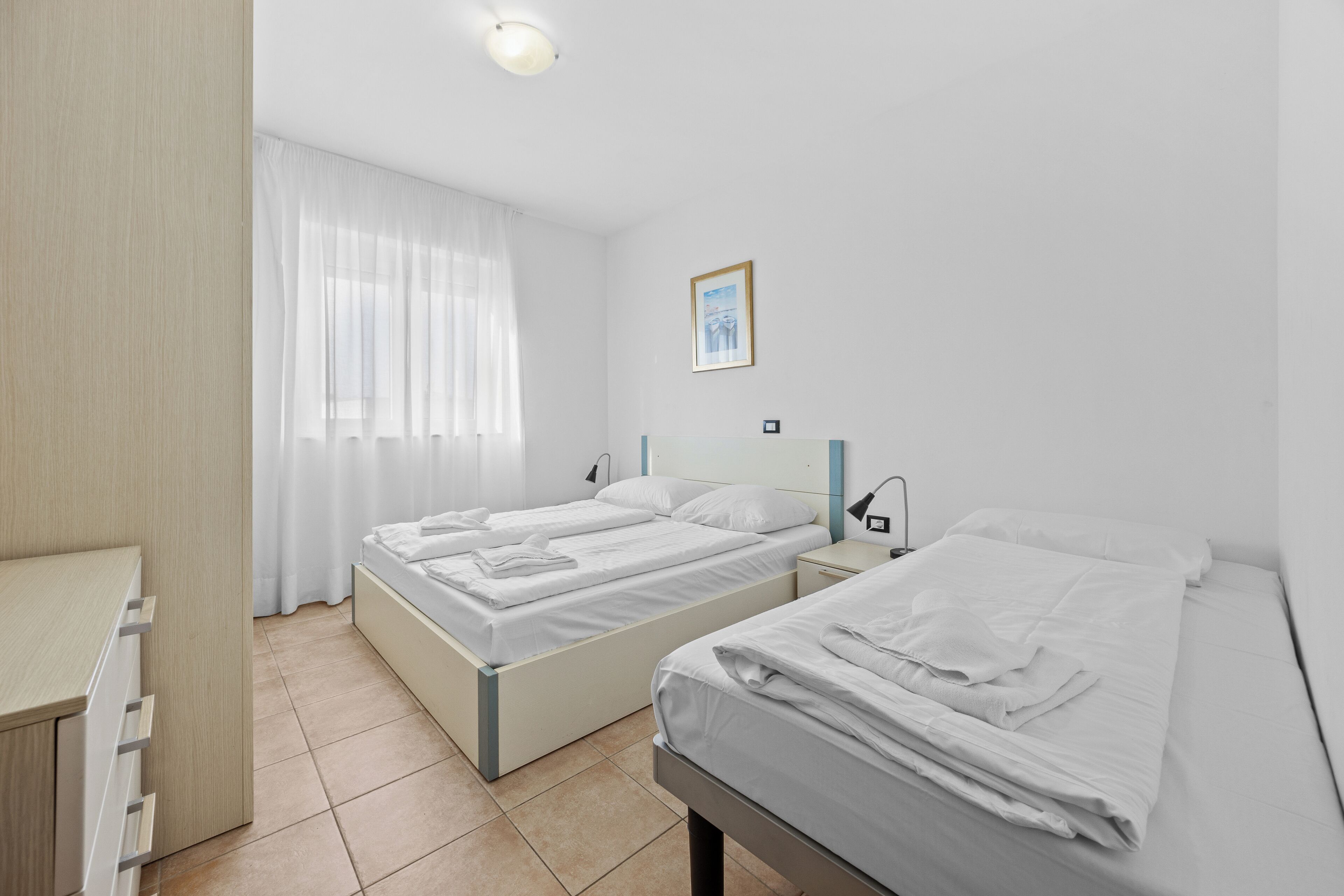Quarto de hotel moderno e limpo, com duas camas de solteiro, uma escrivaninha e uma janela grande com cortinas finas.