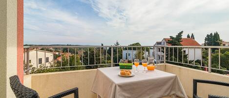 A balcony with a table set for breakfast, including croissants, orange juice, and a green container.