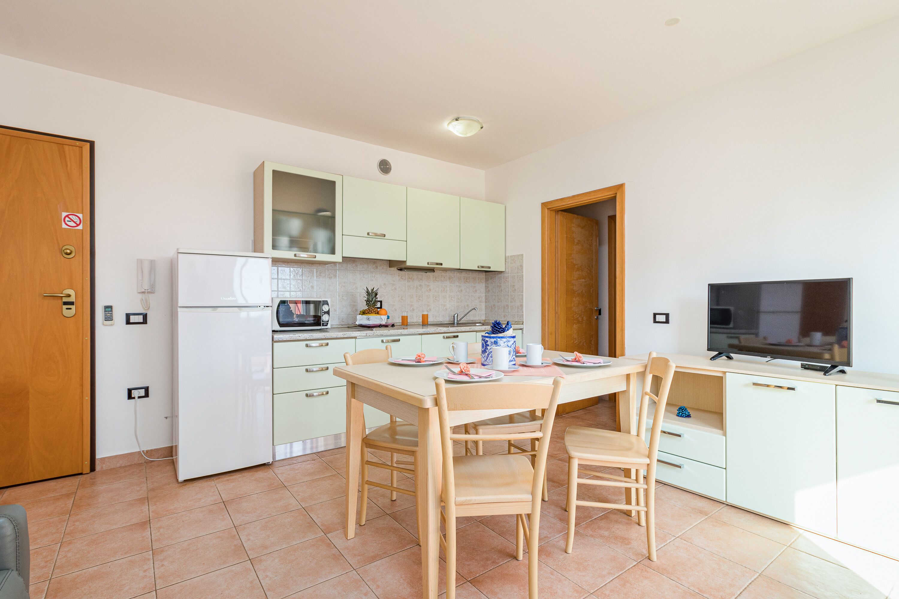 A compact kitchen with a dining table, chairs, a refrigerator, a microwave, a stove, and a television.