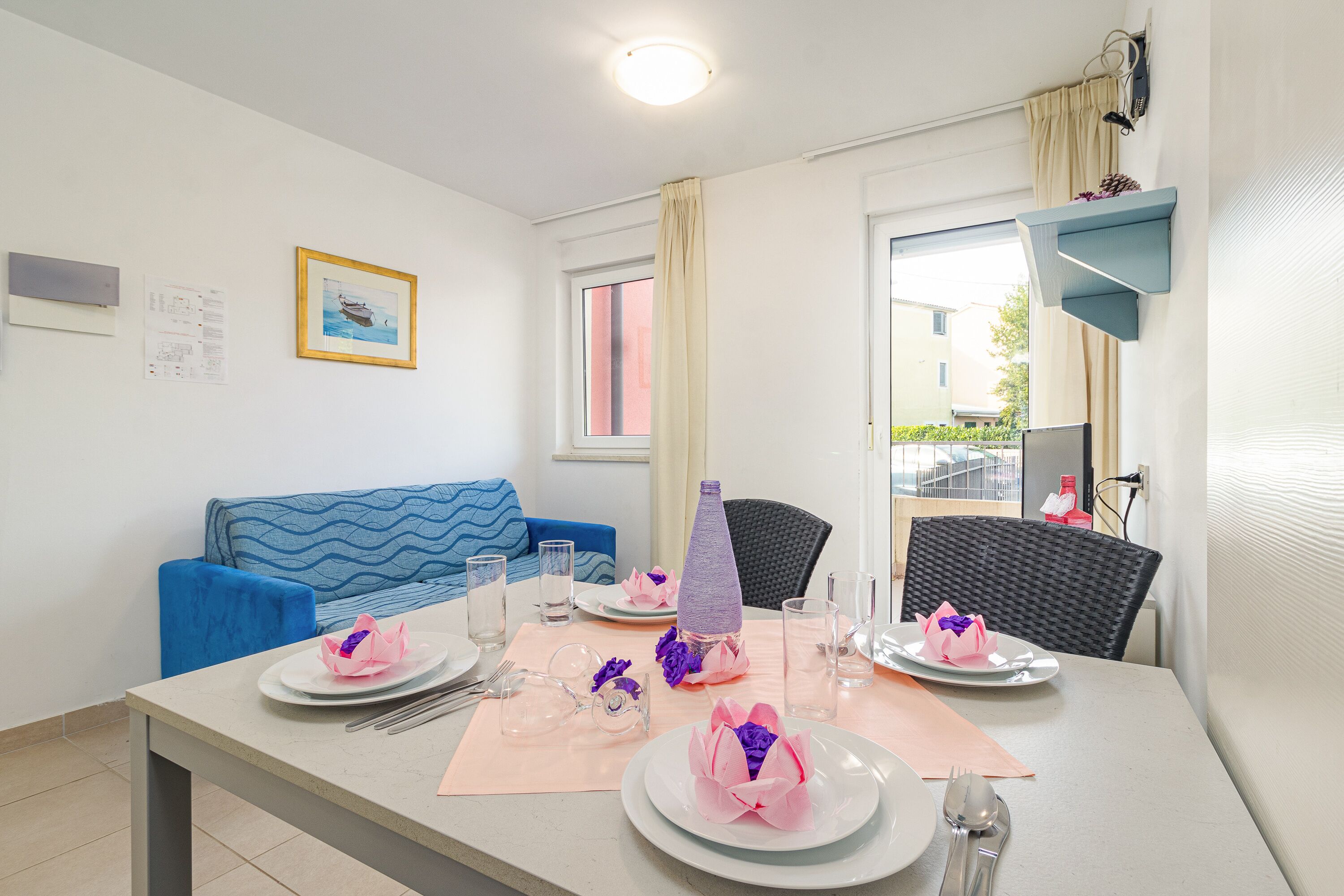 A dining area with a table set for four, a blue sofa, and a window with curtains.