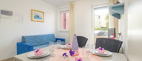 A dining area with a table set for four, a blue sofa, and a window with curtains.
