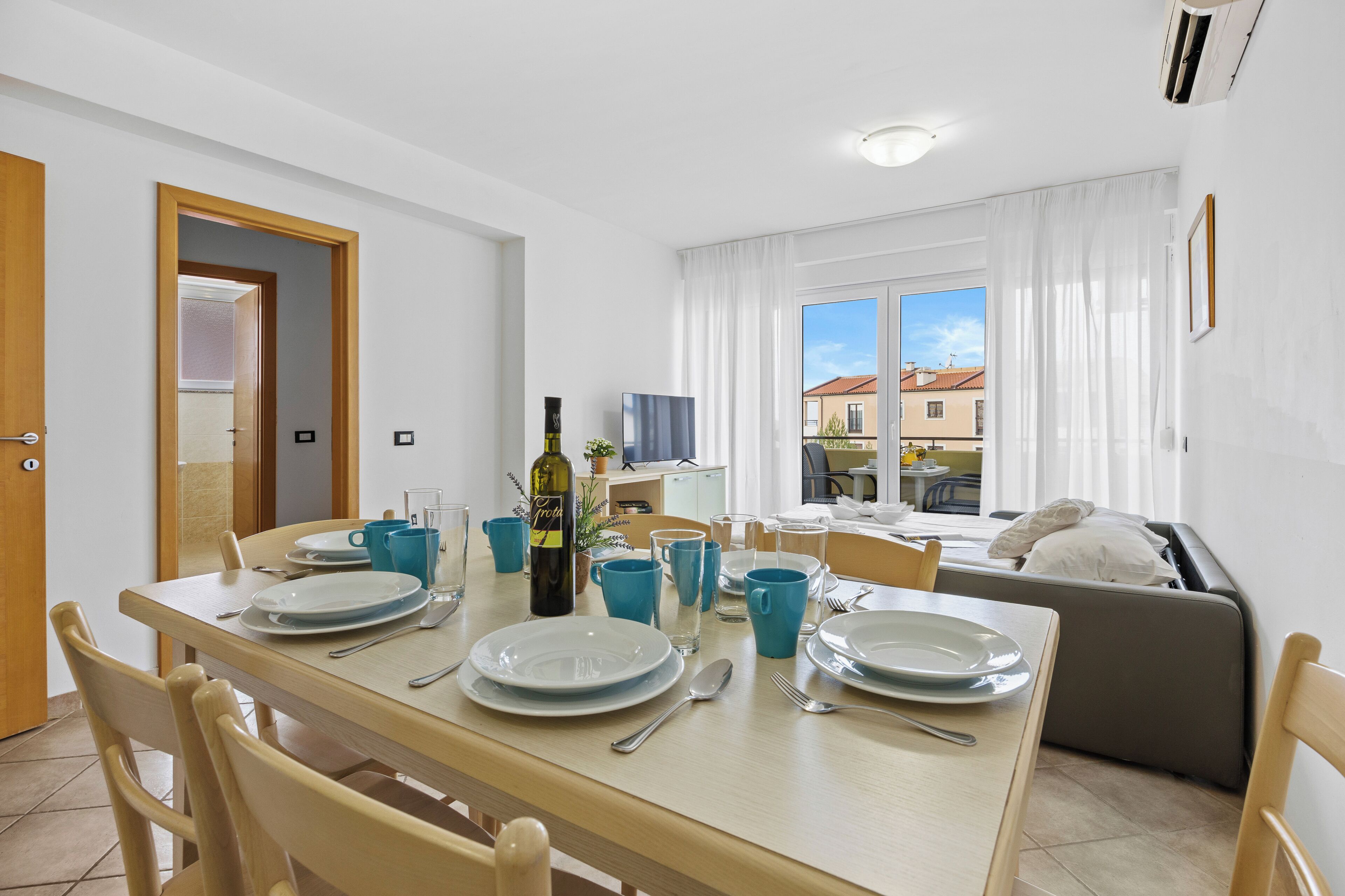 Un coin repas avec une table dressée pour quatre personnes, une bouteille de vin et des tasses bleues.