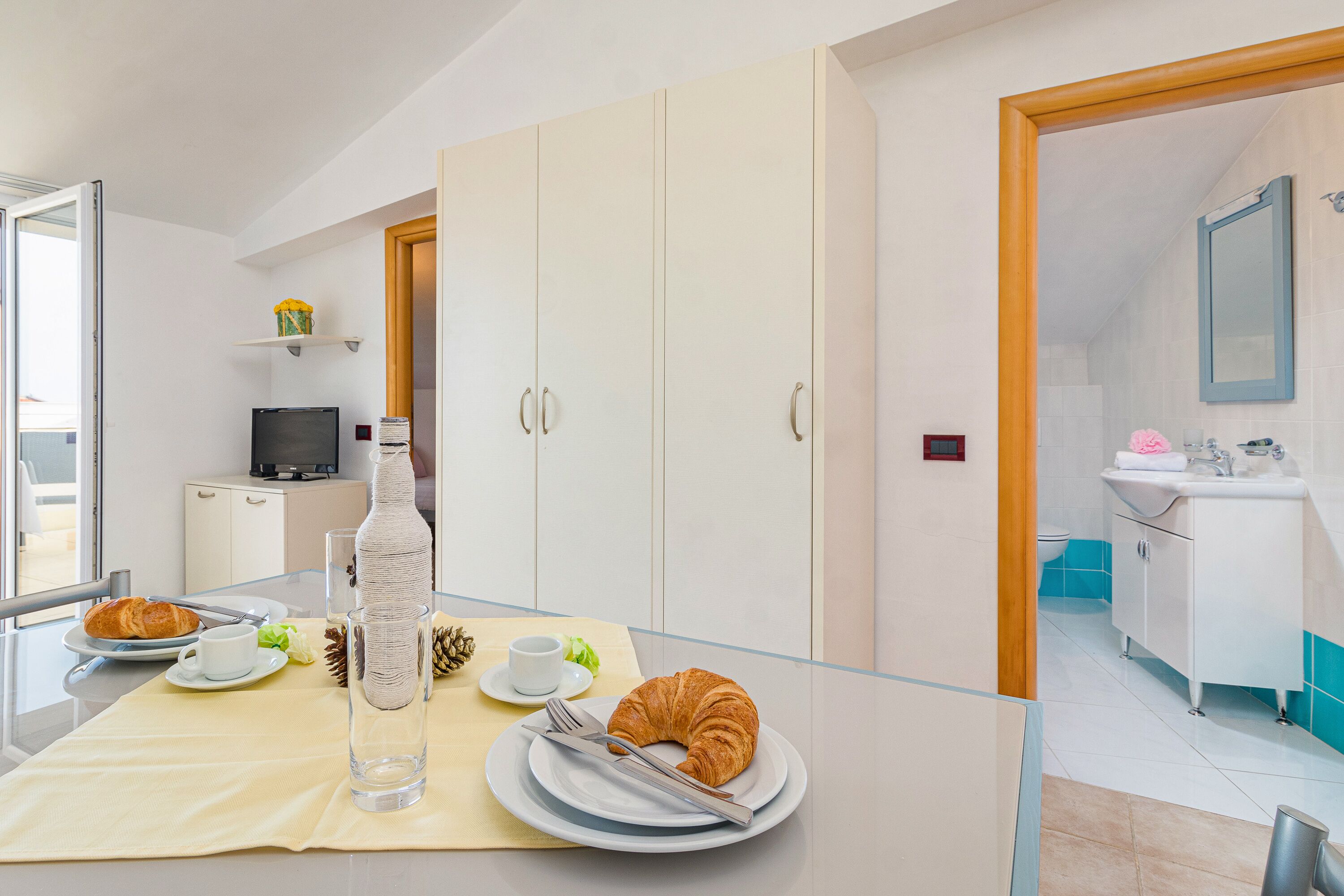 Een moderne hotelkamer met een eethoek, compleet met een tafel, borden, een croissant, een fles en een beker.