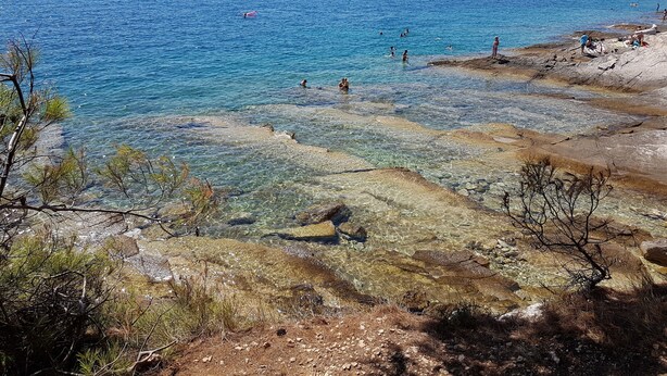 A rocky shoreline with clear water and people swimming. - Residence Kamenjak (Medulin)