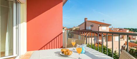 Un balcón con una mesa dispuesta para el desayuno, con cruasanes y zumo de naranja, con vistas a una zona residencial.