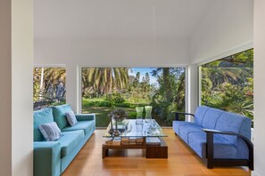 Un saló modern amb una taula de centre de vidre, dos sofàs i vista a un jardí exuberant.