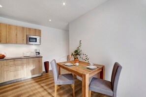 A modern kitchen with wooden cabinets, a microwave, and a dining table set for two with chairs.