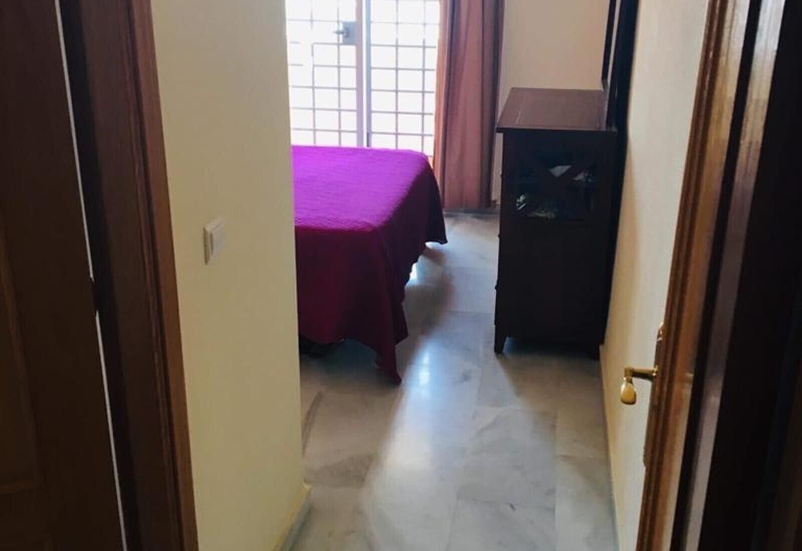 A narrow hallway leading to a room with a bed and a dark wooden cabinet.