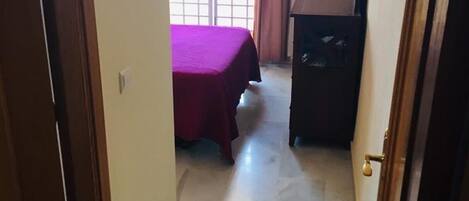 A narrow hallway leading to a room with a bed and a dark wooden cabinet.