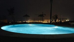 En oplyst swimmingpool med udsigt til bybilledet i baggrunden.