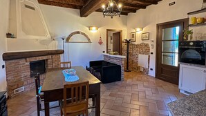 A rustic kitchen with a stone fireplace, wooden ceiling beams, and a dining area with a table and chairs. - Appartamento in storica Cascina Lombarda Cusago (Cascina Cusago di Sotto)