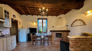 A rustic kitchen with a tiled floor, wooden ceiling beams, a dining table with chairs, a television, and a brick fireplace. - Appartamento in storica Cascina Lombarda Cusago (Cascina Cusago di Sotto)