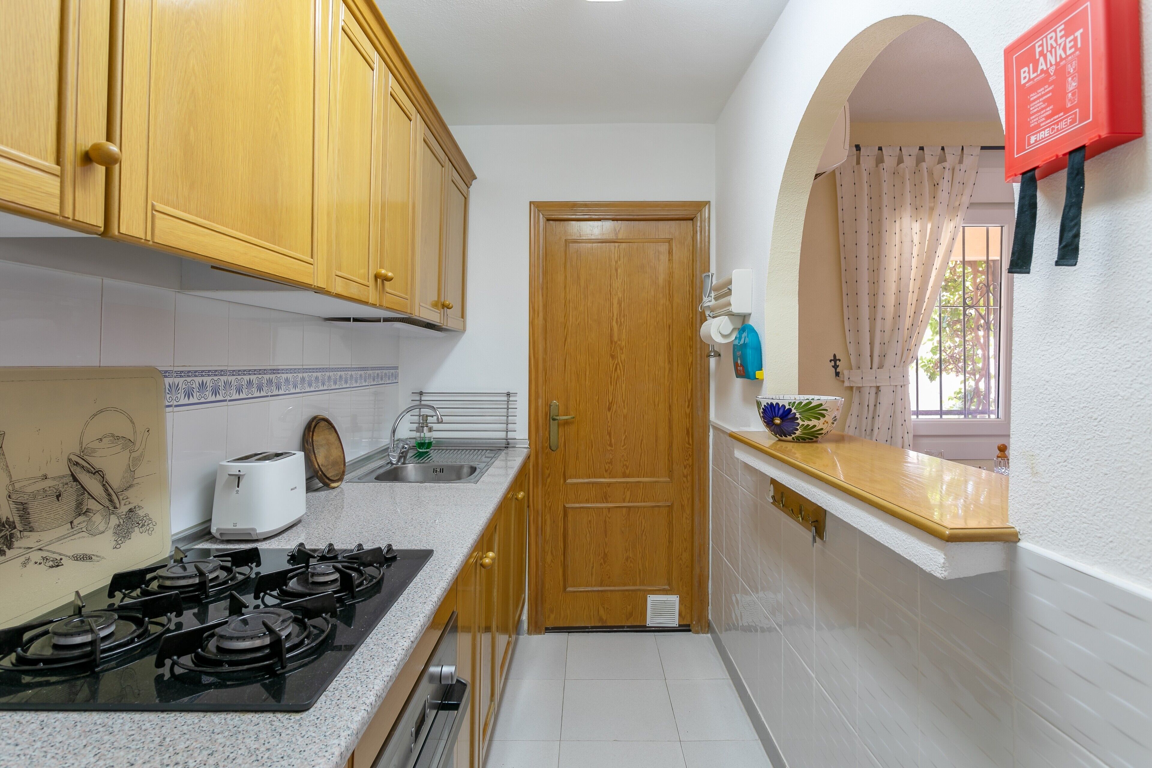 Una cocina con armarios de madera, una estufa a gas, un tostador y un lavamanos.