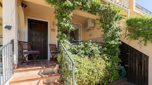 Un bâtiment avec un escalier menant à une porte, un banc et un espace jardin agrémenté de plantes grimpantes.
