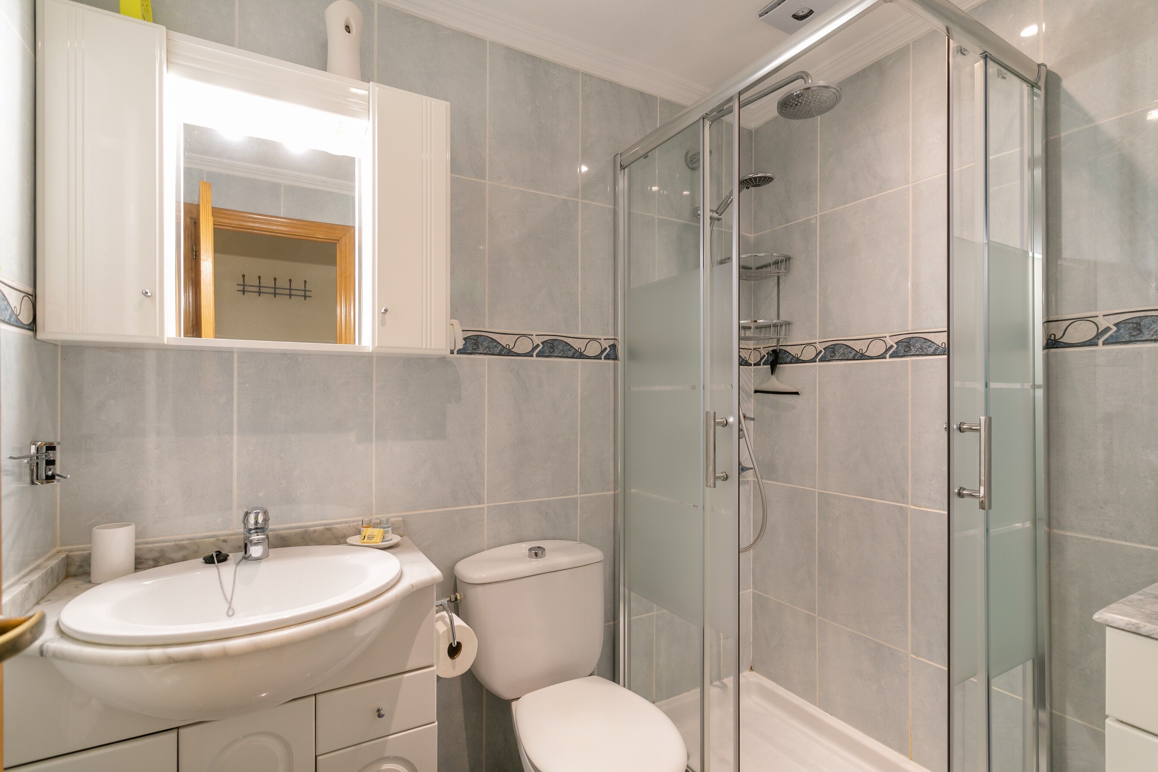 A bathroom with a glass shower enclosure, a sink, a toilet, and a cabinet with a mirror.