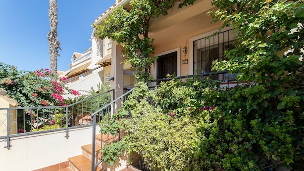 Un immeuble résidentiel doté d’un escalier, d’un balcon et d’un jardin où poussent des fleurs roses.