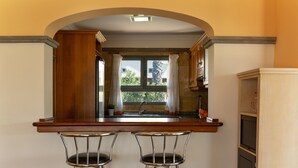 Une cuisine avec une fenêtre, deux tabourets de bar et un four encastré.