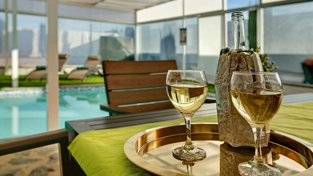 A glass of white wine on a tray with a bottle of wine, a bench, and a pool in the background. - Vacation home 'Los Cipreses' with Mountain Views, Indoor Pool, Garden & Wi-Fi (Ingenio)