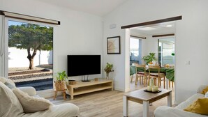 A modern living room with a flat-screen TV, a sofa, a coffee table, and a dining area with a table and chairs. - Vacation home 'Los Cipreses' with Mountain Views, Indoor Pool, Garden & Wi-Fi (Ingenio)