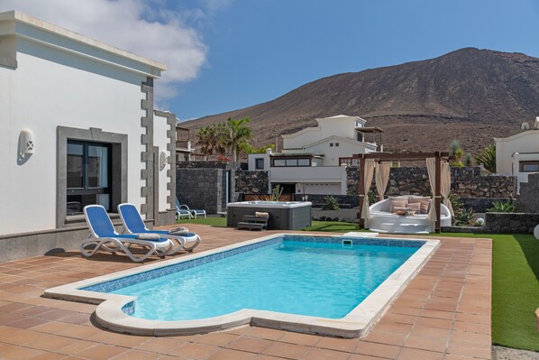 A swimming pool with lounge chairs, a hot tub, and a stone wall.