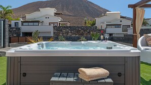 A hot tub with a towel, surrounded by a stone wall, with a mountain in the background. - Villa Los Alisios 58 with Mountain Views, Pool, Wi-Fi, Terraces and Garden (Playa Blanca)