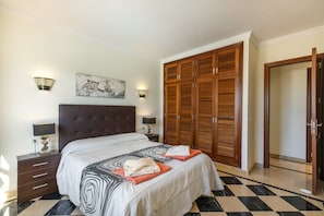 A bedroom with a large bed, a wardrobe, a nightstand, and a wall-mounted lamp.