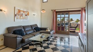 A living room with a checkered floor, a leather sofa, a glass coffee table, and a view through a glass door. - Villa Los Alisios 58 with Mountain Views, Pool, Wi-Fi, Terraces and Garden (Playa Blanca)